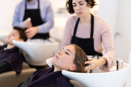 Young woman stylist washes female clients hair, prepares it for cutting and stylingの写真素材