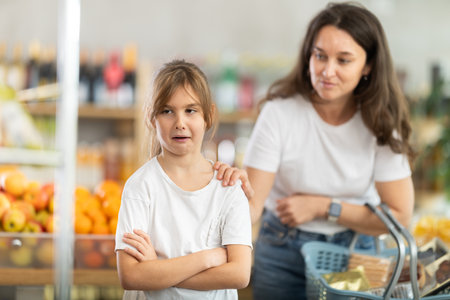 Mom calms down her capricious daughter who wants to buy sweets at supermarketの写真素材