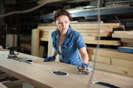 During manufacturing, woman employee grinds surface of wooden board, gives smoothness to surface