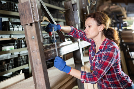 Female employee of workshop stands next to iron rails of workpieces, measures length