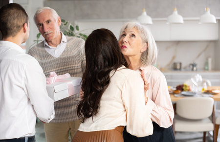 Happy senior man and woman welcoming young couple at home