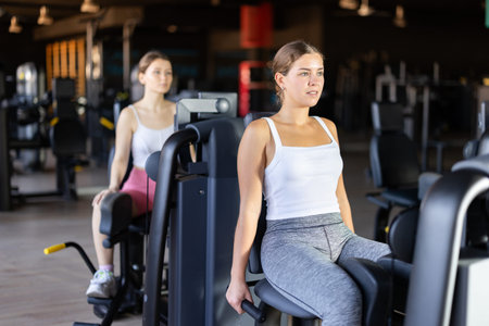 Slender athletic girl work out muscles of legs and thighs on simulator in fitness club
