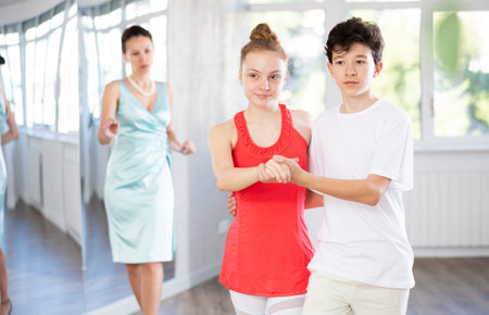 Dance lesson - teacher teaches teenage girl and boy to dance tango in studio