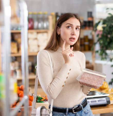 Young woman choosing raw sausages in grocery storeの写真素材