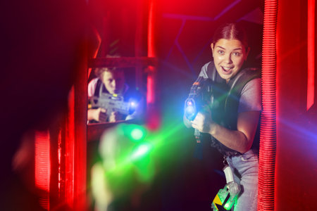 Joyous girl with laser pistol playing laser tag with friends on labyrinthの写真素材