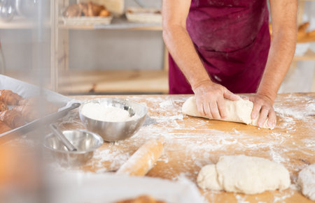 Elderly baker hands kneading dough on table, closeup