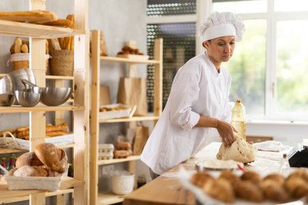 Woman works in bakery as baker, kneads dough, works with flour.の写真素材