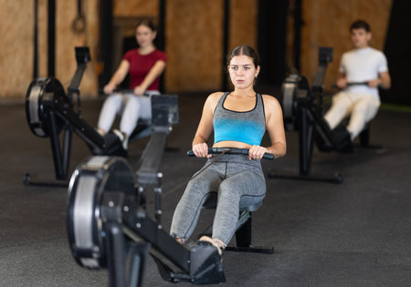 Focused girl works out with rowing machine during class at fitness club