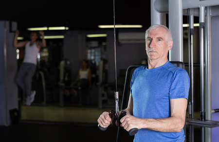 Mature man in sportswear training on rope loop simulator in gym