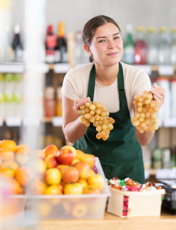 Store employee offering fresh grapes at produce counterの写真素材