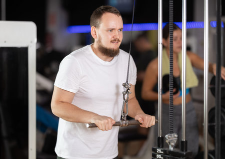 Man in gym performs exercises for arm muscles using cable crossover machine and pull weighted rope