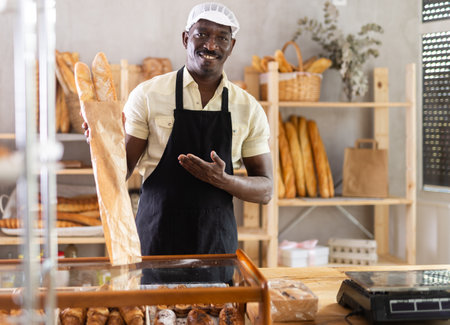 Portrait of male baker with bread and baguettes in hands in bakeryの写真素材