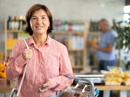 Visiting store, elderly woman is looking at something on shelf of showcase. Man buyer in backgroundの写真素材