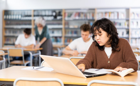 Focused asian teenager female student sitting at library desk, preparing for examの写真素材