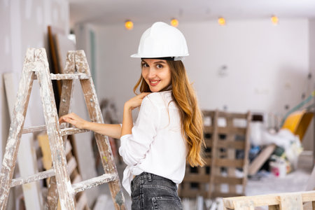 Attractive girl in construction helmet, denim shorts and unbuttoned shirt posing in room under reconstructionの写真素材