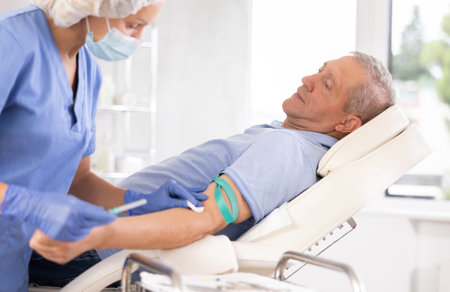Old man having vein injection lying on clinical chairの写真素材