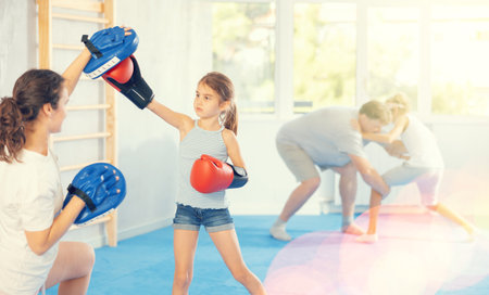 Girl and mom are boxing in gym, mother helps child to work out force of blow.の写真素材
