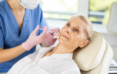 Professional cosmetologist performing lip filler injections to senior womanの写真素材