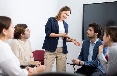 Positive successful female teacher listening to answers from students of different ages while they sitting in circle at foreign language lessonの写真素材