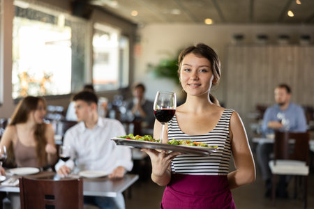 Waitress standing with salad and glass of wine on serving tray in restaurantの写真素材