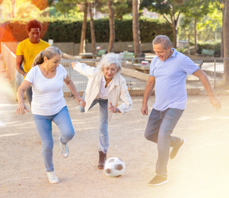 Cheerful group of mixed-race middle-aged and older adult people playing football game outdoorsの写真素材