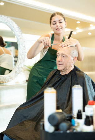 Young female hairdresser working with scissors and comb with mature manの写真素材