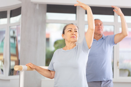 Elderly women and men practice at ballet standing in fourth position at barre in choreography studioの写真素材