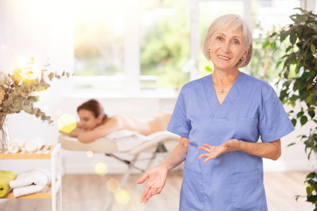 Female elderly physiotherapist poses against background of spa salons office.の写真素材