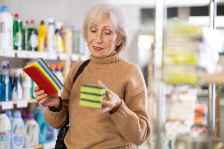 Positive mature woman choosing cleaning sponge in department storeの写真素材