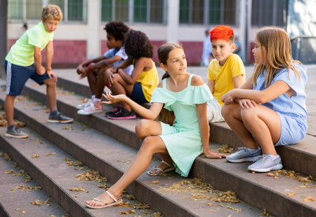Happy tweenagers friends sitting on steps outdoors and chatting