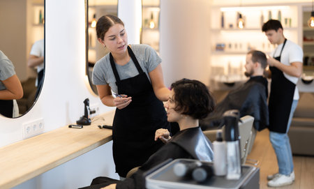 Young female hairdresser giving haircut to adult womanの写真素材