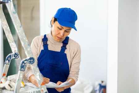 Woman foreman in overalls signs an act of acceptance of completed work indoorの写真素材