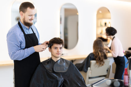 Young man barbershop employee stands next to male client, discussing details of haircutの写真素材