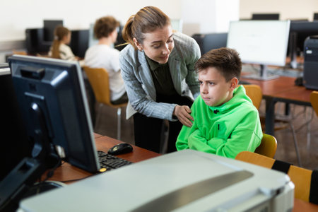 Caring female teacher calming upset tween schoolboy in computer classの写真素材