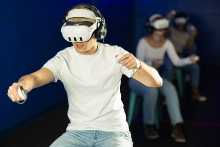 In darkened hall of gaming club, guy in VR helmet takes part in group game