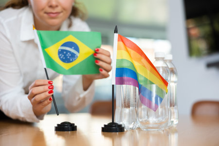 Young woman putting Brazil and LGBT flags on table in officeの写真素材