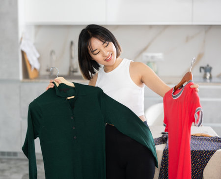 Happy young Asian girl trying to choose a dress in the kitchenの写真素材