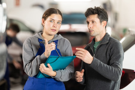 Girl employee asks clarifying questions and writes down male clients wishes regarding car repairsの写真素材