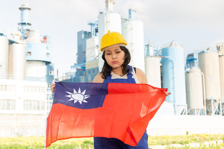 Worried asian girl in work clothes and hardhat standing in front of industrial sceneryの写真素材