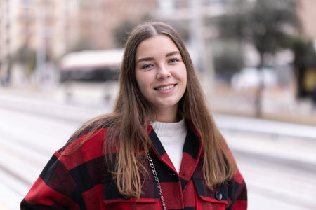 Girl is standing on street platform, waiting for tram to arrive