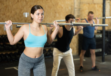 Motivated CrossFit female athlete lifting heavy body bar or barbell during group training in gym. Functional training concept.の写真素材
