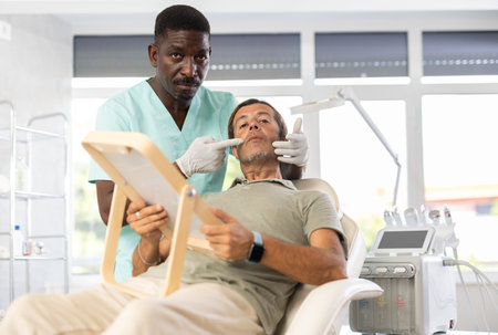 African male cosmetologist examines face of man patient and consult on possibility of rejuvenationの写真素材
