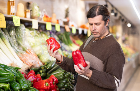 Adult man chooses peppers in vegetable shopの写真素材