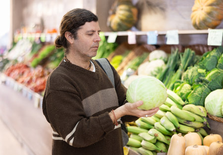 Adult man chooses cabbage in vegetable shopの写真素材