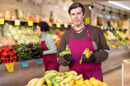 Adult man seller puts bananas on displayの写真素材