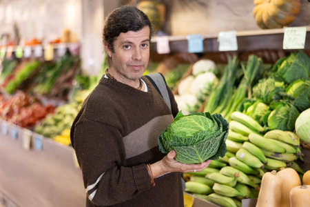 Adult man chooses cabbage in vegetable shopの写真素材