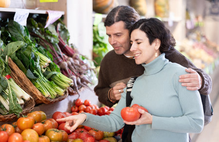 Couple man and woman choosing tomatoes in vegetable shopの写真素材