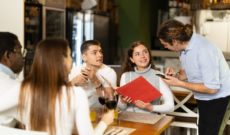 Man waiter writes down girls order. Employee serve couple clients in cafeの写真素材