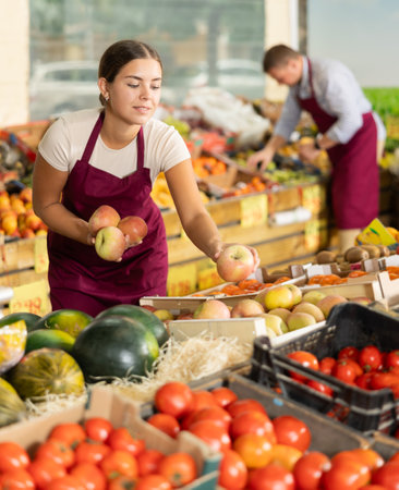 Young salesgirl laying out fresh apples for sale in greengroceryの写真素材