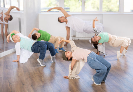 Preteen boys and girls studying movement of contemporary dance in classroom with his friends